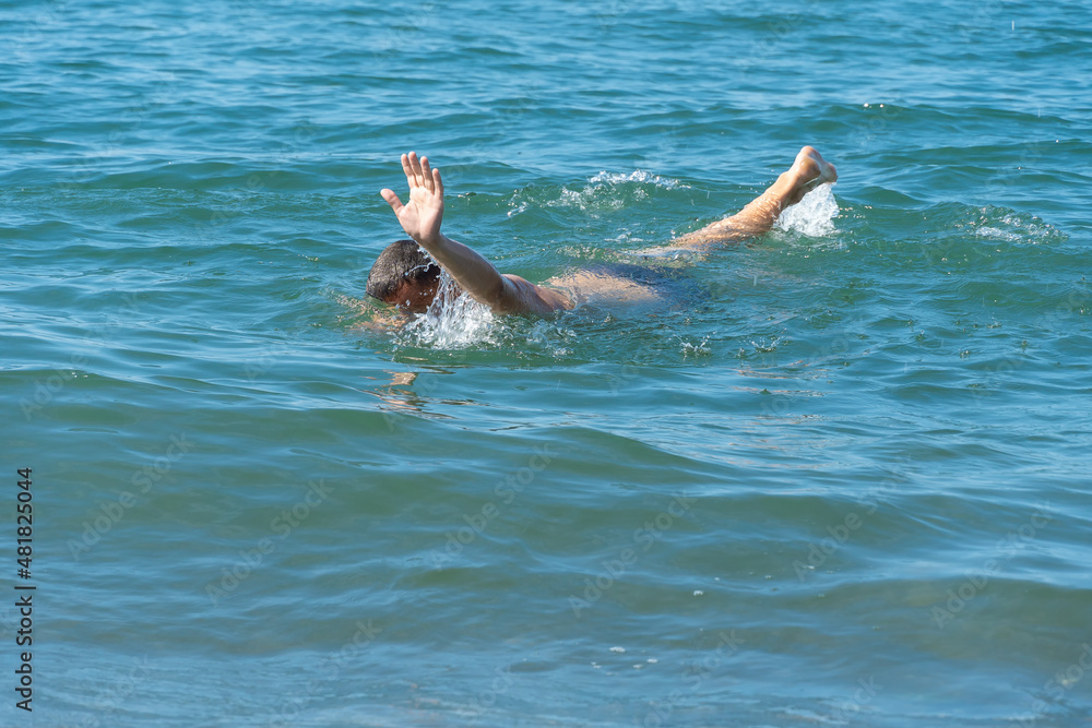 Man drowns in the sea on a sunny day, trying to ask for help with his hand