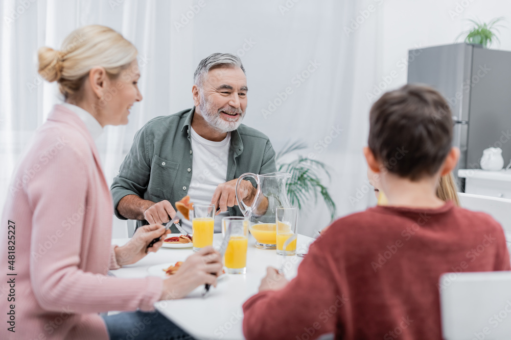 cheerful senior man having breakfast with blurred grandchildren and wife in kitchen. cheerful senior man having breakfast with blurred grandchildren and wife in kitchen.