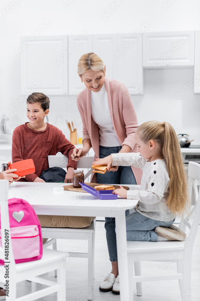 Obraz premium happy middle aged woman preparing sandwiches with chocolate paste for grandchildren.