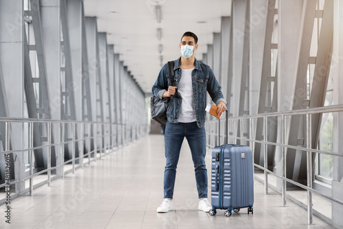 Coronavirus Travels. Young Middle-Eastern Man In Medical Mask Standing In Airport Terminal