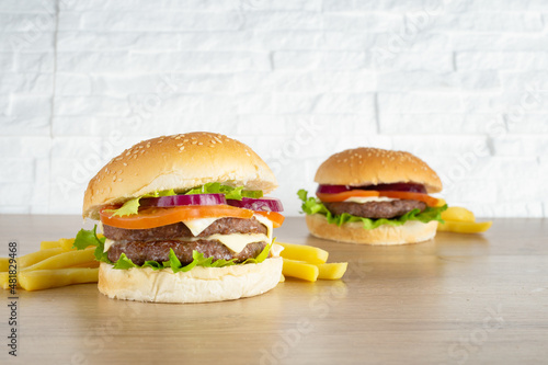 Hamburger and double burger with meat, salad, cheese, tomato and onion on wooden top and with white brick background