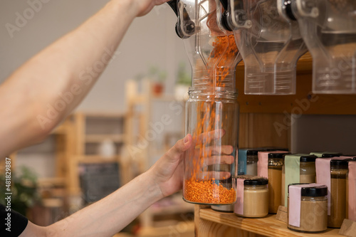 A man fills a jar with red lentils. Selling bulk goods by weight in an eco store. Trade concept without plastic packaging photo
