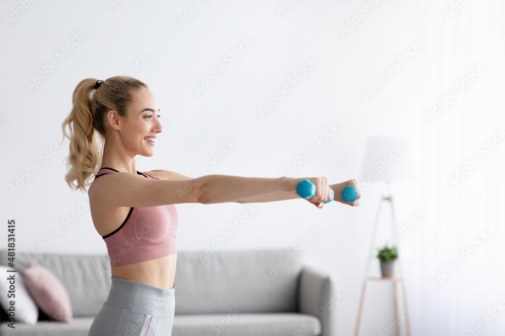 Happy caucasian pretty young blonde lady lifting dumbbells at home in domestic gym, side view Happy caucasian pretty young blonde lady lifting dumbbells at home in domestic gym, side view