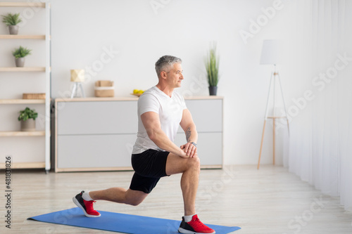 Home fitness. Motivated mature man doing lunges in living room interior, free space, banner design