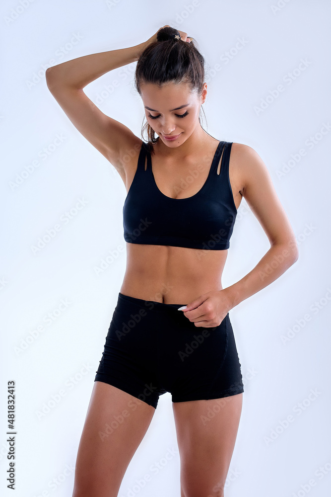 Amusing fintess lady in black top holding long hair in ponytail over white background in studio. good-looking pretty woman preparing for sport exercises. Healthy lifestyle, sport, wellbeing concept