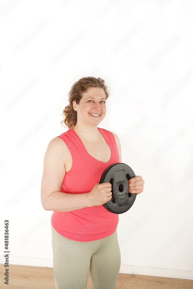 Frau macht Fitness, hat Hantelscheibe in der Hand, heller Hintergrund Frau macht Fitness, hat Hantelscheibe in der Hand, heller Hintergrund