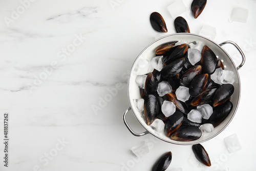 Colander with raw mussels and ice on white marble table, flat lay. Space for text