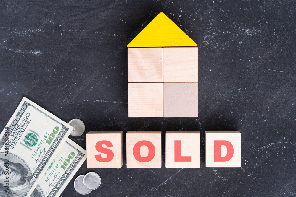 Sold. The word sold on wooden cubes, a house made of wooden blocks and dollar bills on a black background Sold. The word sold on wooden cubes, a house made of wooden blocks and dollar bills on a black background