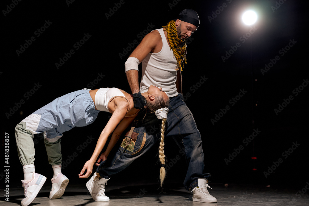 couple of male and female dancing hip-hop in casual clothes on black background at dance hall, on stage. Youth culture, hip-hop, movement, style and fashion, action. Fashionable portrait. couple of male and female dancing hip-hop in casual clothes on black background at dance hall, on stage. Youth culture, hip-hop, movement, style and fashion, action. Fashionable portrait.