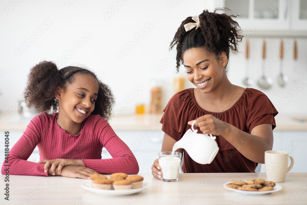 Pretty black mother pouring fresh milk for her teen daughter