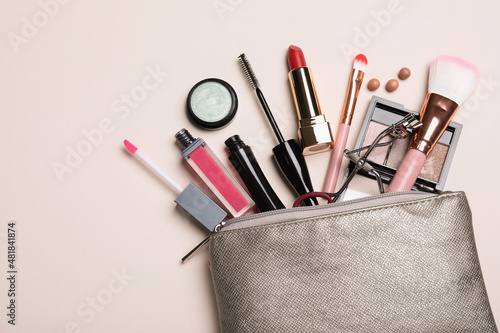 Cosmetic bag with makeup products and accessories on beige background, flat lay