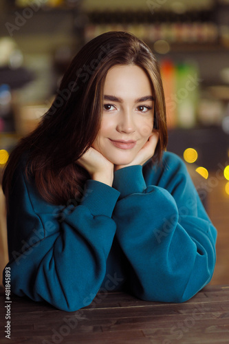 Portrait of a beautiful young girl in a blue hoodie sitting at a cafe table.