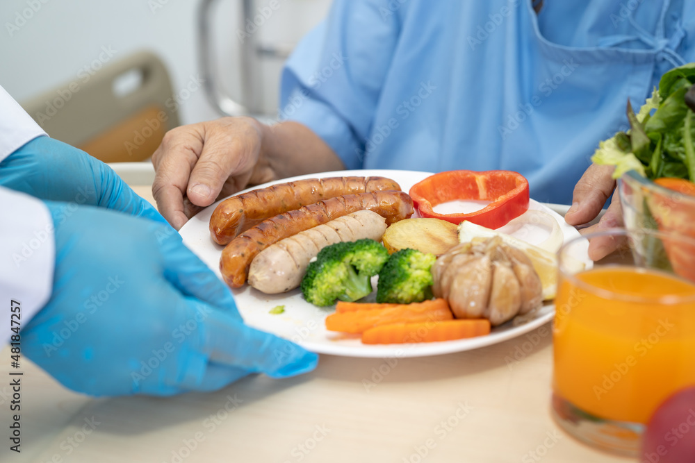 Asian senior or elderly old lady woman patient eating breakfast and vegetable healthy food with hope and happy while sitting and hungry on bed in hospital.