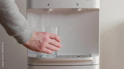 The man takes a glass of water from the water dispenser. Clean water for healty life.