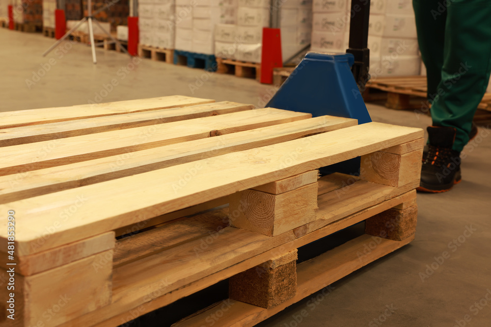 Worker moving wooden pallets with manual forklift in warehouse, closeup Worker moving wooden pallets with manual forklift in warehouse, closeup