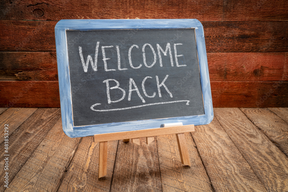 welcome back - white chalk handwriting on a slate blackboard, easel sign against rustic, weathered wood, hospitality and business concept