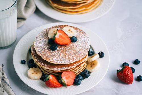 Tasty pancakes with strawberry, blueberry and banana in a white plate on the table.