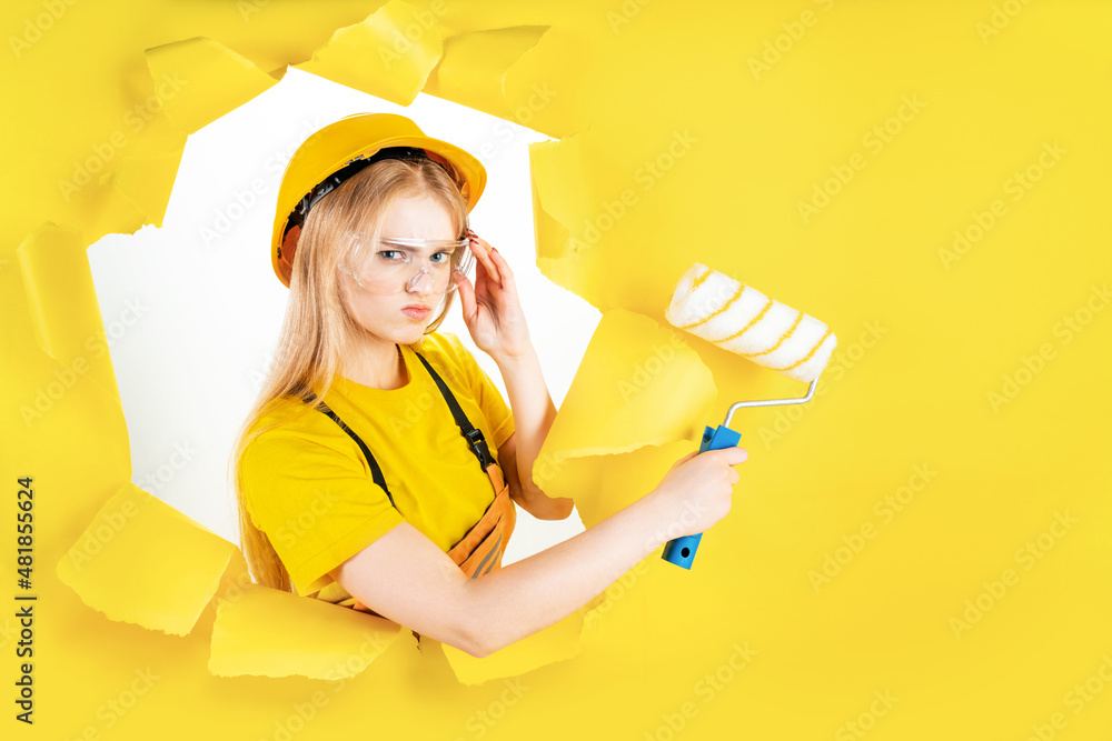 Positive busy female builder involved in renovation and repair of building holds roller and paint brush follows strict safety regulations wears protective equipment has leadership skills. Copy space. Positive busy female builder involved in renovation and repair of building holds roller and paint brush follows strict safety regulations wears protective equipment has leadership skills. Copy space.