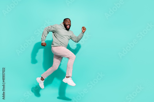 Full length body size view of attractive cheerful trendy guy jumping going copy space isolated over vivid teal turquoise color background