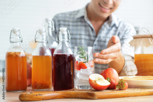Young man recommends Kombucha healthy probiotic fermented tea drinks, ingredients : red apple, strawberries, rosemary and Scoby mushrooms to start the fermentation process nearby, selective focus