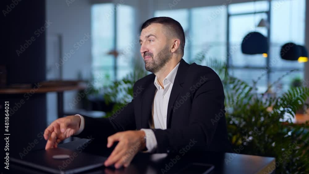 Man in suit sitting at the table and laptop in front of him. Bearded man trying to open computer but fail again and again. Blurred background. Man in suit sitting at the table and laptop in front of him. Bearded man trying to open computer but fail again and again. Blurred background.