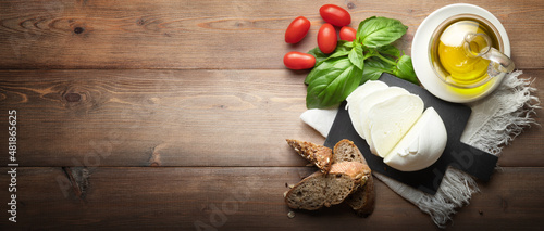 Fotografie Buffalo mozzarella, bread, cherry tomatoes, extra virgin olive oil and basil on wooden background, top view, space for text