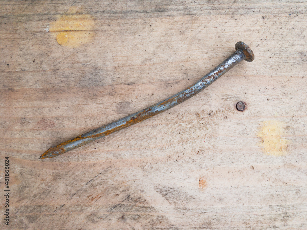 A single rusty used nail on a wooden board