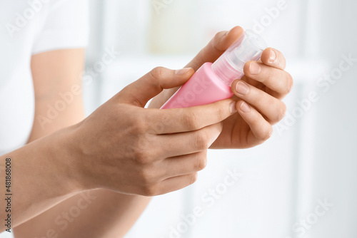 Young woman holding bottle of cosmetic lotion at home  closeup
