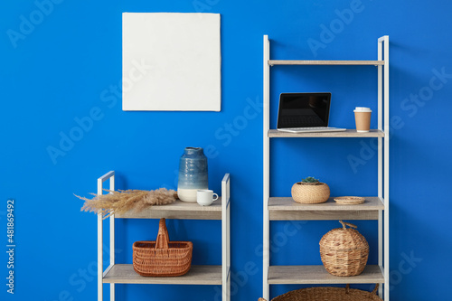 Shelving unit with decor, laptop computer and cups of coffee near blue wall