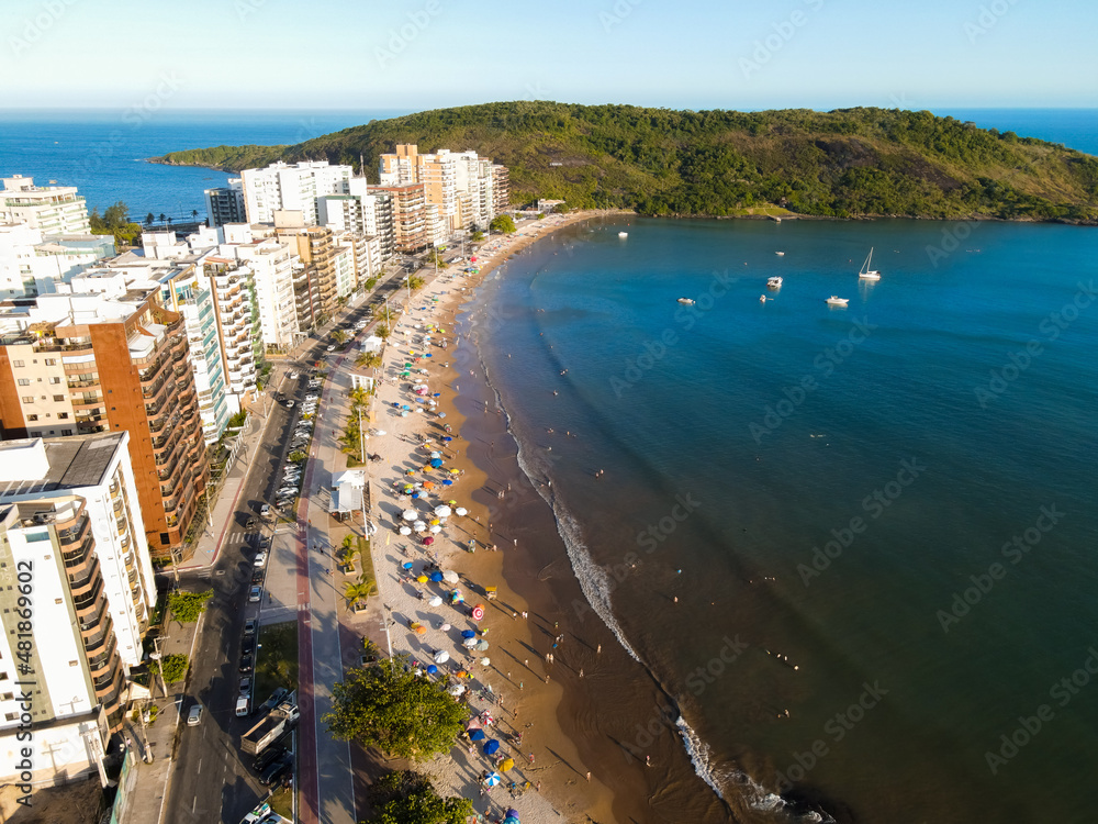 Imagem de drone da Praia do Morro em Guarapari num dia ensolarado com muitas pessoas se divertindo, aproveitando o dia na praia e praticando esportes.