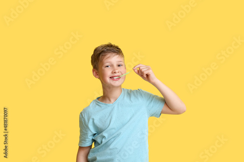 Obraz na plátně Little boy in blue t-shirt chewing gum on yellow background