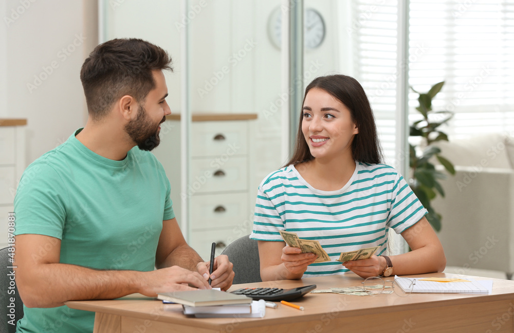 Happy young couple counting money at wooden table indoors Happy young couple counting money at wooden table indoors