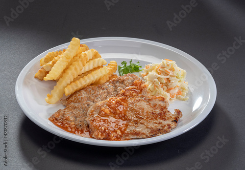 Grilled pork chop with spicy salad and french fries in white dish on dark grey background