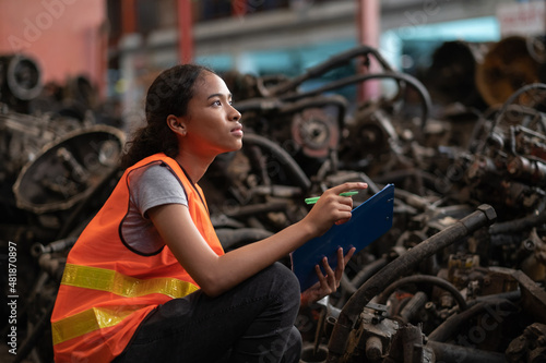 Africa American worker woman standing in the automotive engine part at the factory with copy space. Holding clipboard and checking inventory of old engine in garage. Industrial and stock concept.