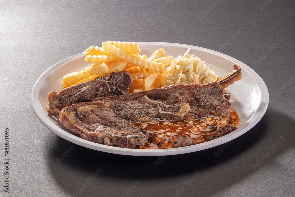 Organic Grilled Lamb Chop sauce with french fries and salad in white dish on dark grey background top view Organic Grilled Lamb Chop sauce with french fries and salad in white dish on dark grey background top view