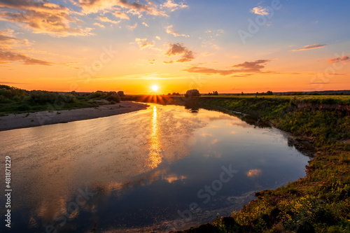 Amazing view at scenic landscape on a beautiful river and colorful sunset with reflection on water surface and glow on a background, spring season landscape
