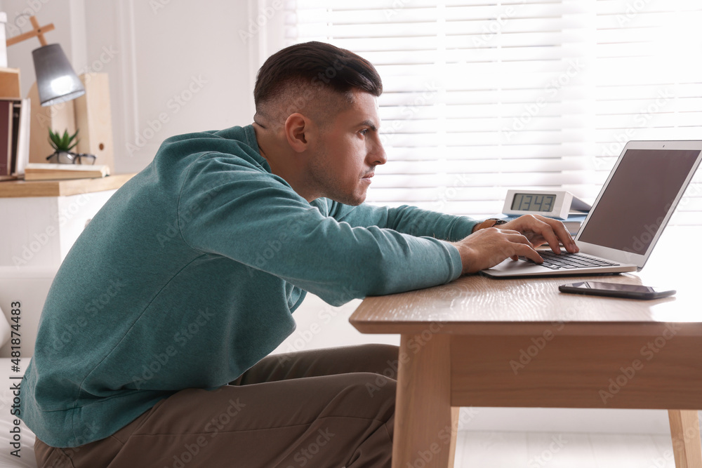 Man with poor posture using laptop at table indoors - obrazy, fototapety, plakaty 
