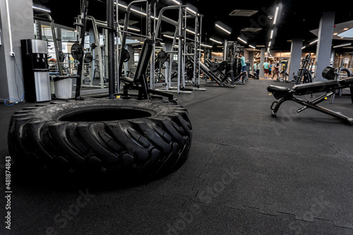 Fitness wheel from a tractor for crosfit, against the background of the sports hall of the simulators in a black background