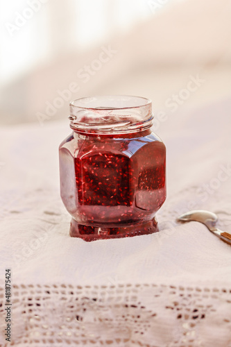 Homemade jam in a glass and fresh raspberry on white embroidered table cloth. Preserved berries. Copy space