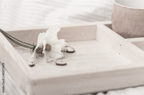 White flowers, cup of coffee or tea, hearts on a wooden tray in bed, copy space. Coffee in bed, relaxing morning concept