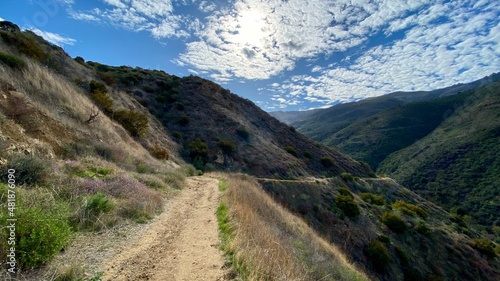 Hiking trail leading down to a winding section through Santa Monica Mountains at Point Mugu State Park, California. Lots of small clouds in sky