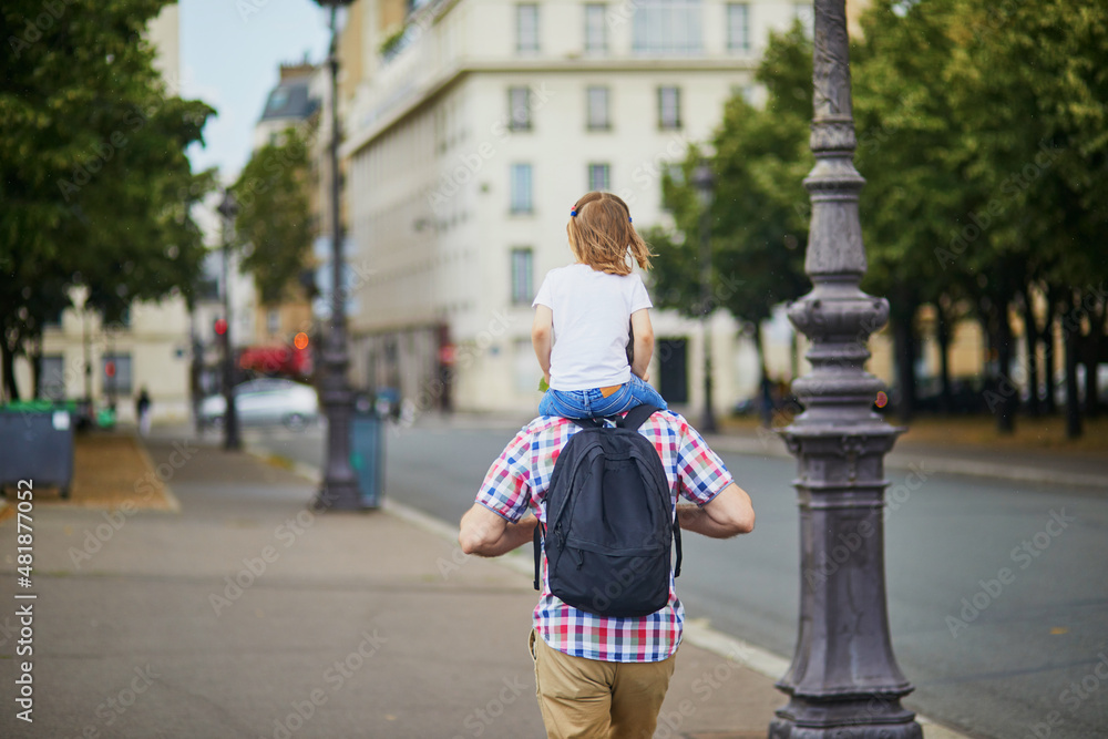 Father holding his daughter on shoulders and walking on a street of Paris