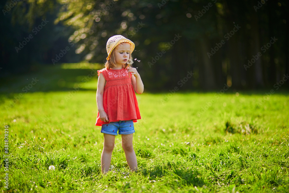 Little girl in straw hat blowing on dandelion on a summer day Little girl in straw hat blowing on dandelion on a summer day