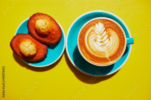 Cup of fresh flay white coffee with milk drawing in blue cup on yellow table