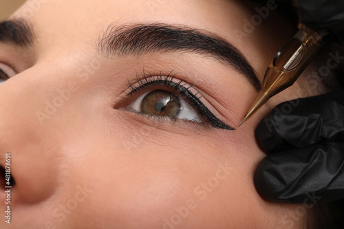 Young woman undergoing procedure of permanent eye makeup in tattoo salon, closeup photo