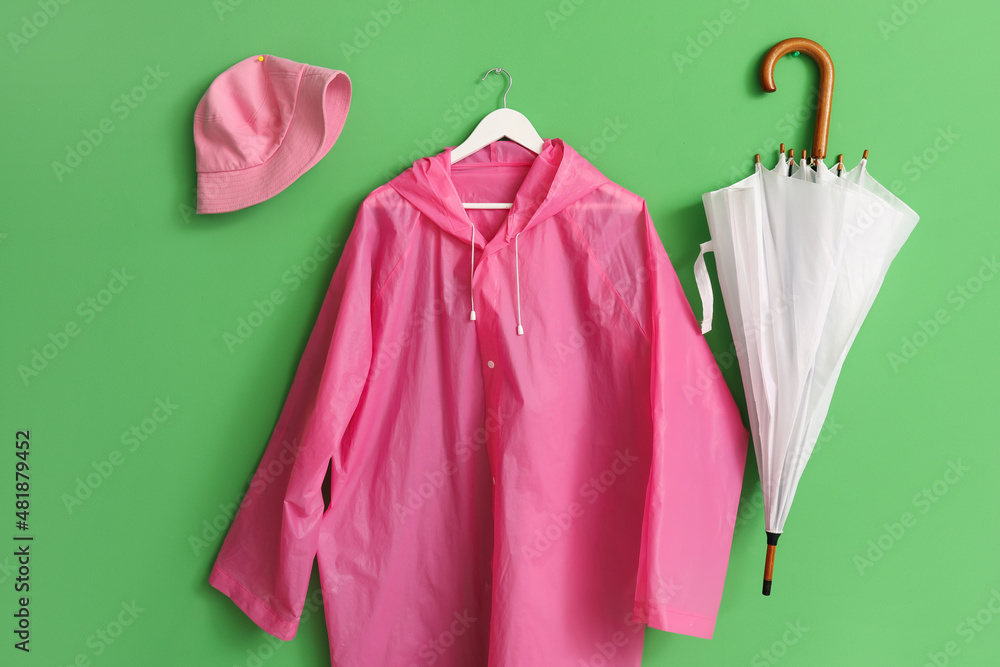 Pink raincoat with hat and umbrella hanging on green wall Pink raincoat with hat and umbrella hanging on green wall