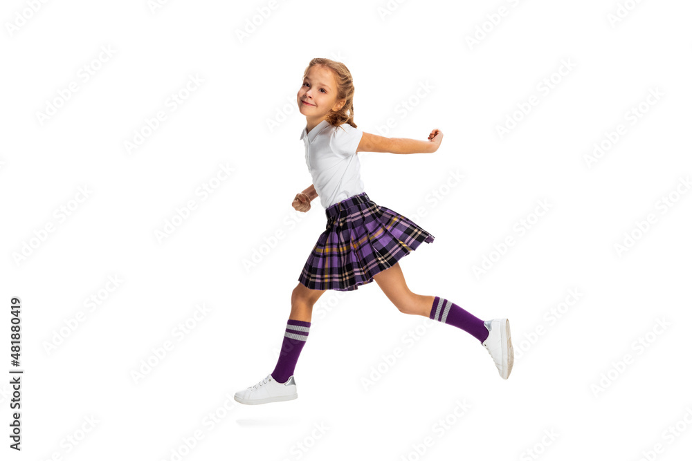 Portrait of cute little girl, pupil in school uniform running isolated on white background. Concept of childhood, emotions, study