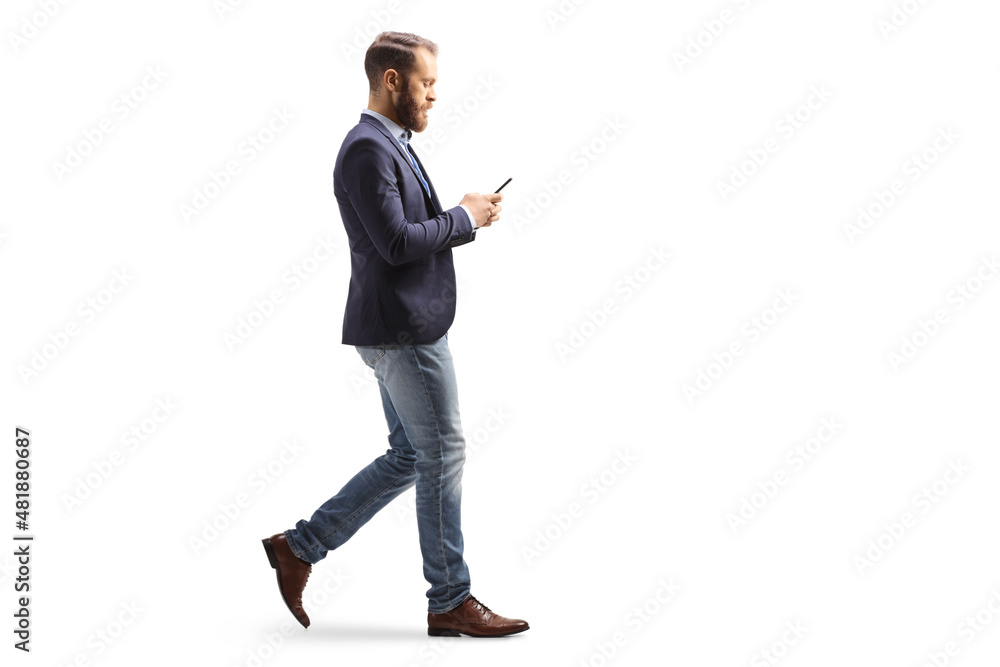 Full length profile shot of a young man in suit and jeans walking and typing on a mobile phone - obrazy, fototapety, plakaty 