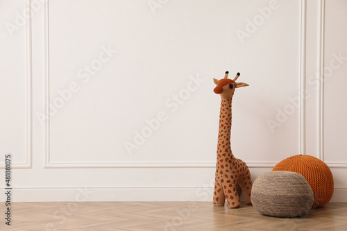 Toy giraffe and poufs near white wall indoors, space for text. Interior design
