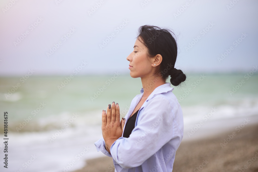 Beautiful portrait of young woman doing yoga or meditating on the seaside. Yoga sport. Healthy wellness lifestyle. Spiritual health. Personal fulfillment.